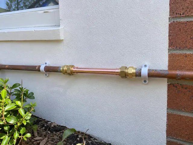 Repaired copper water pipe on an exterior rendered wall beside a brick corner in Putney
